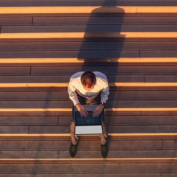 Man sitting on steps using a laptop casting a shadow in the evening sun