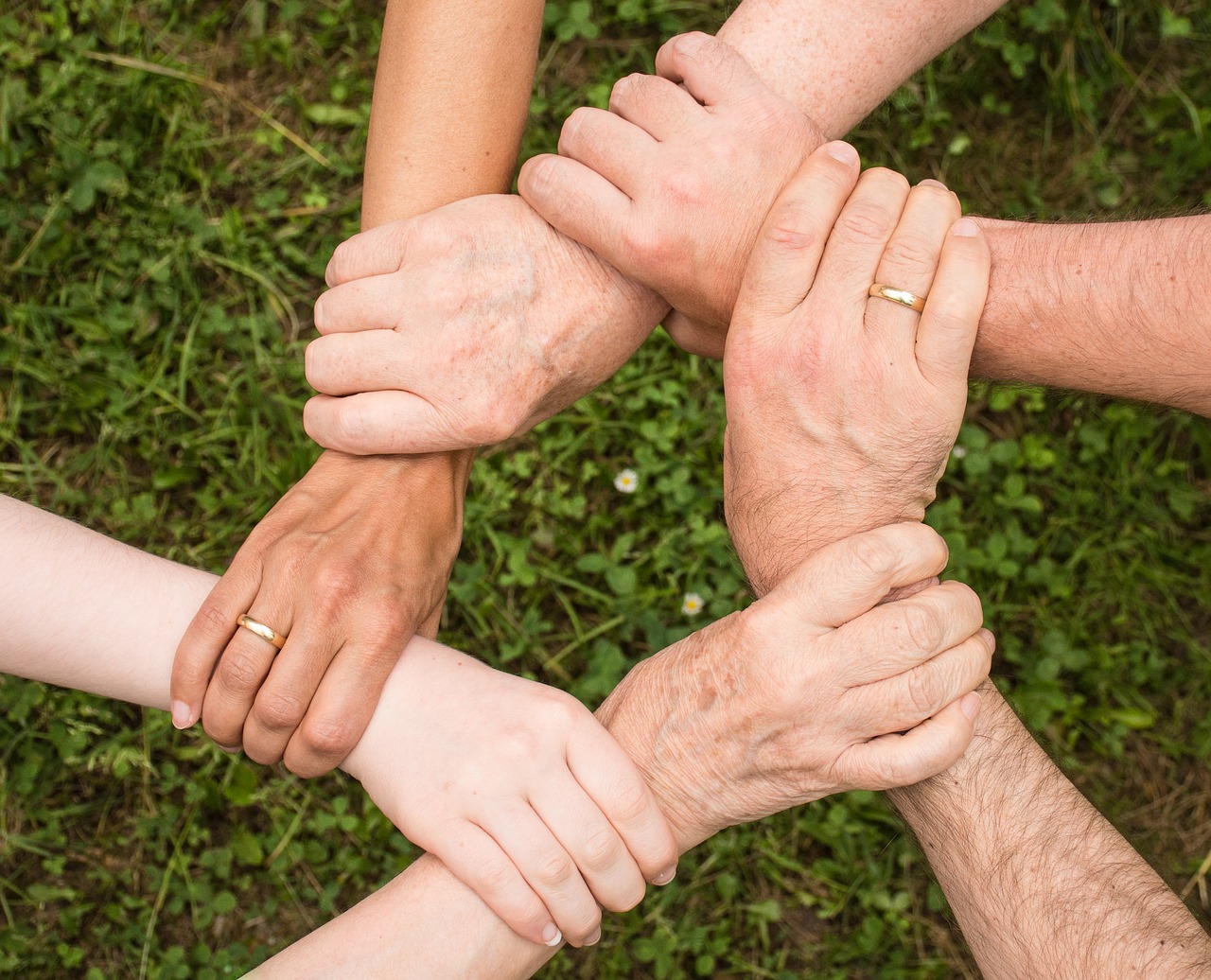 Hexagonal aerial view of six people's hands, each holding the wrist of the person behind them in a circle